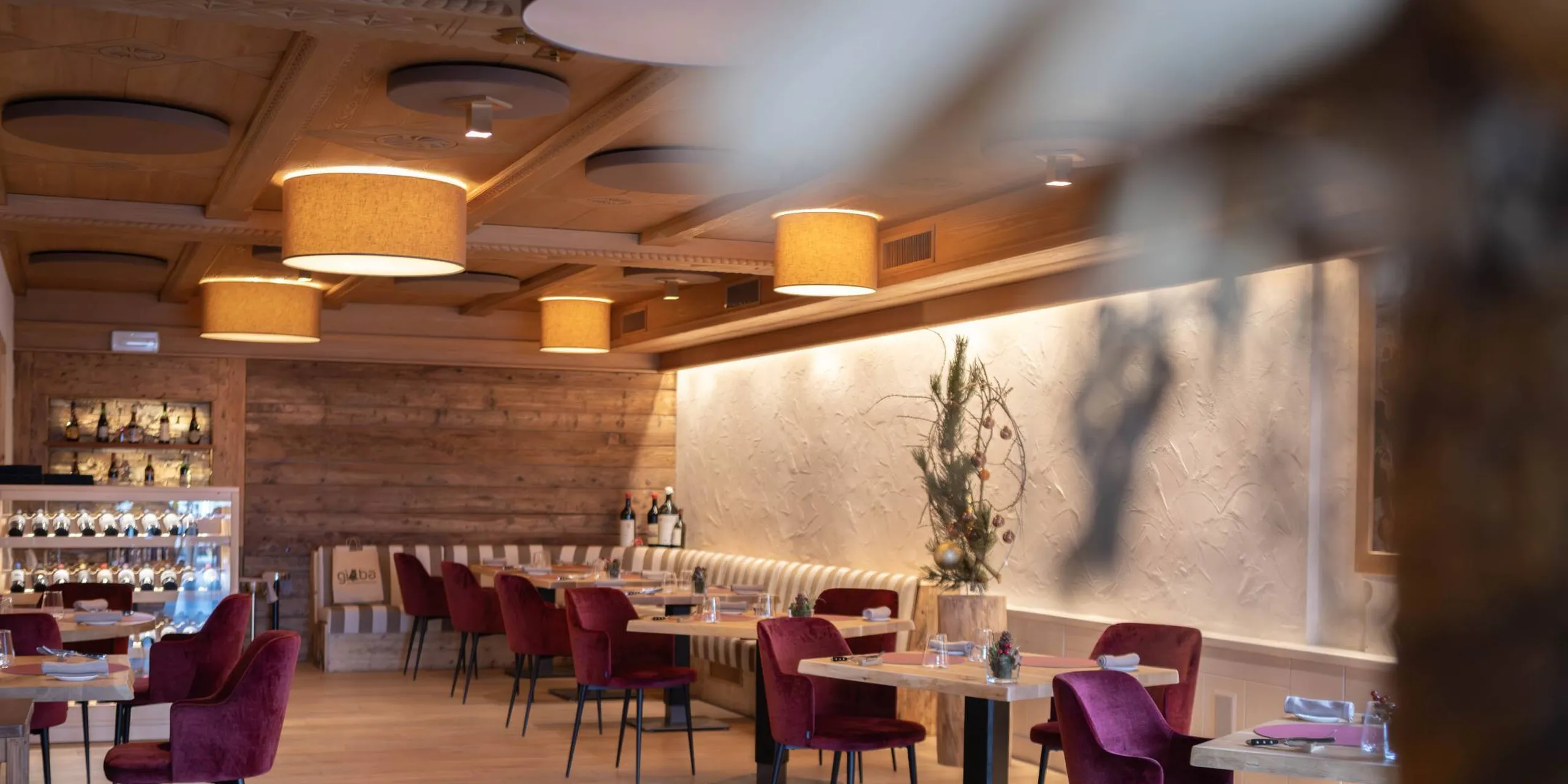 Interno ristorante Silenzia: soffitto in legno, lampade beige, tavoli e sedie rosse, bar a sinistra, decorazioni naturali lungo la parete.