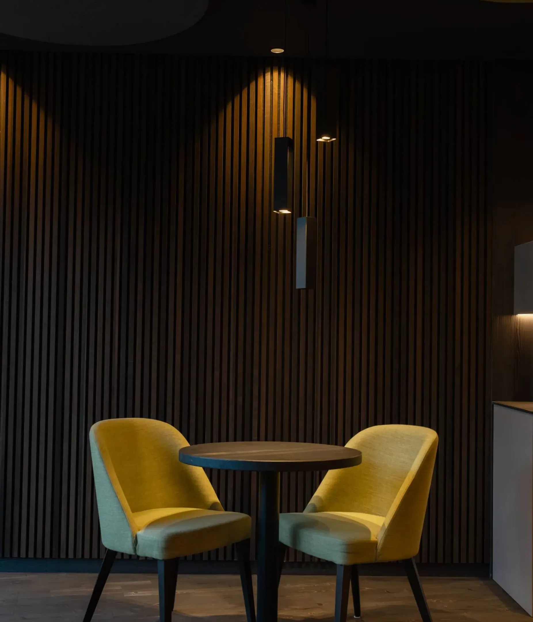 Due poltrone gialle disposte attorno a un tavolo rotondo nero, in una lounge con pannelli fonoassorbenti in legno scuro e luci calde.