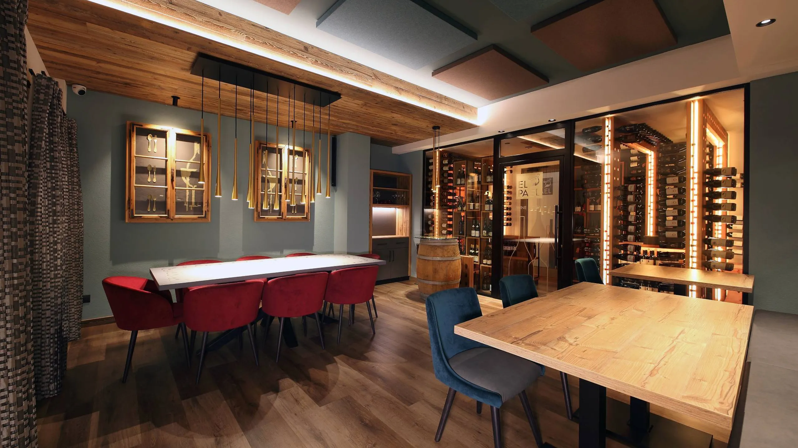 Sala showroom Silenzia: tavolo lungo con sedie rosse a sinistra, area enoteca a vetro con bottiglie illuminate a destra, pavimento in legno e pannelli acustici.