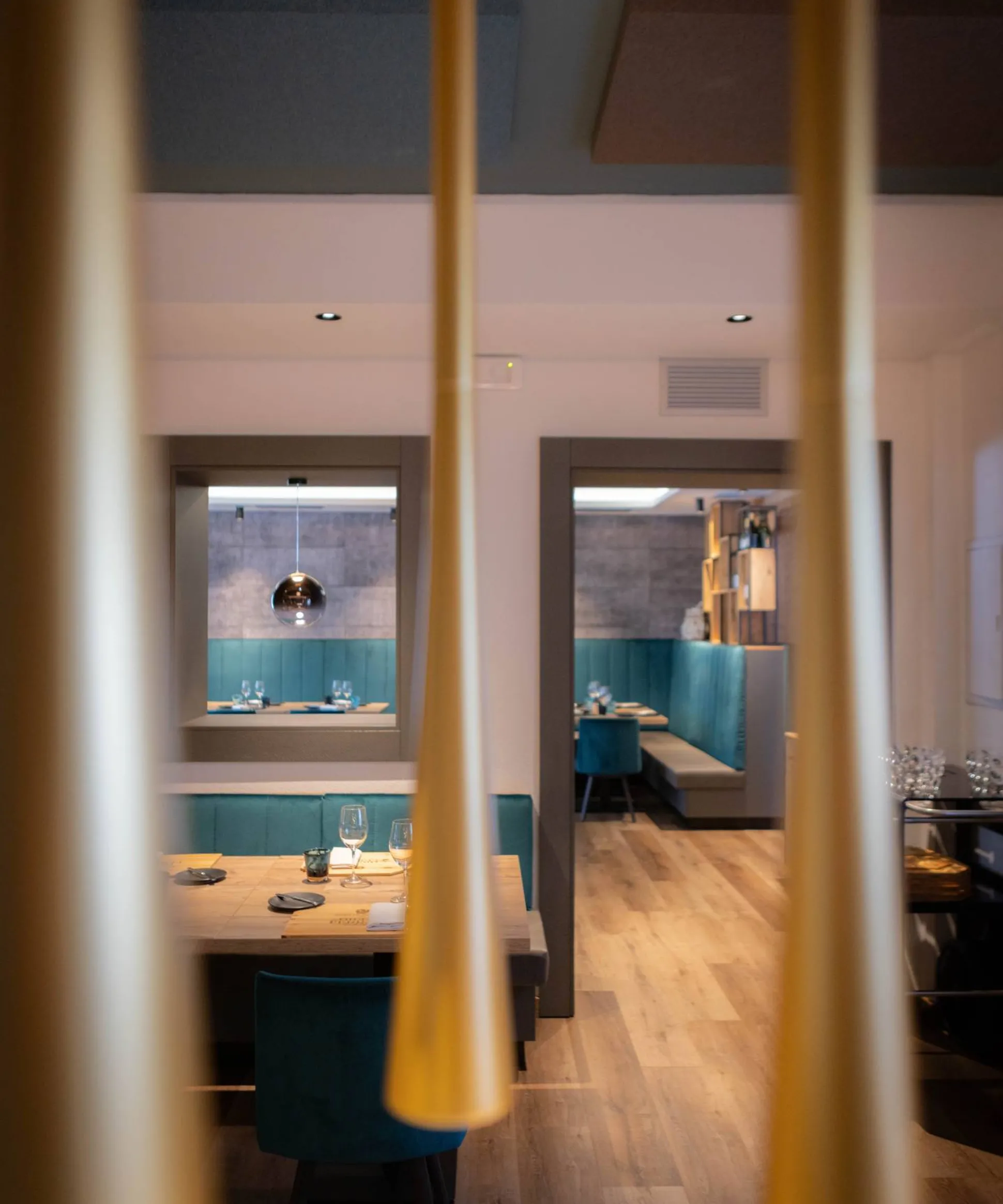 Interno di ristorante moderno con panche blu-turchese, tavoli in legno, pannelli acustici e luci pendenti coniche gialle in primo piano.