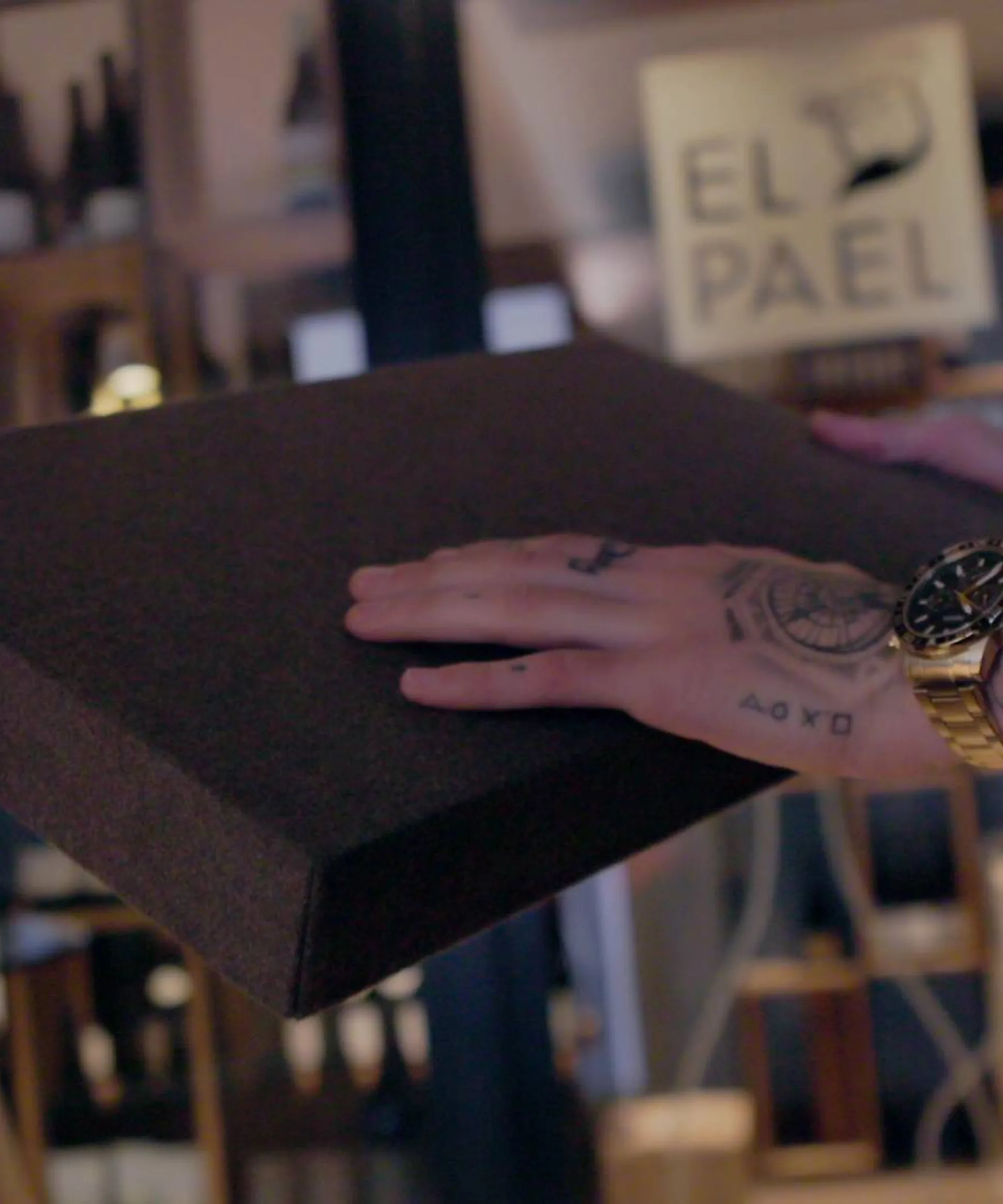 Persona con orologio dorato e tatuaggi sorregge un pannello acustico rettangolare scuro; sfondo showroom Silenzia con vasi decorativi.