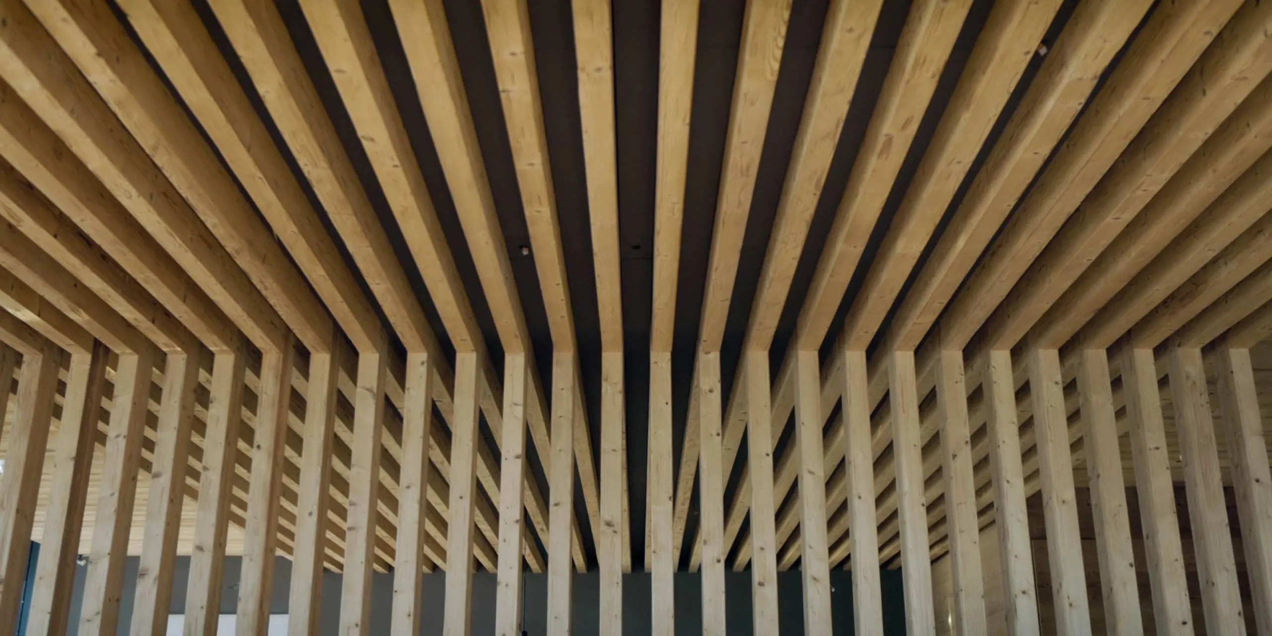 Interno moderno con soffitto a listelli di legno chiaro e montanti verticali di legno, disposti in righe parallele per un effetto acustico architettonico.