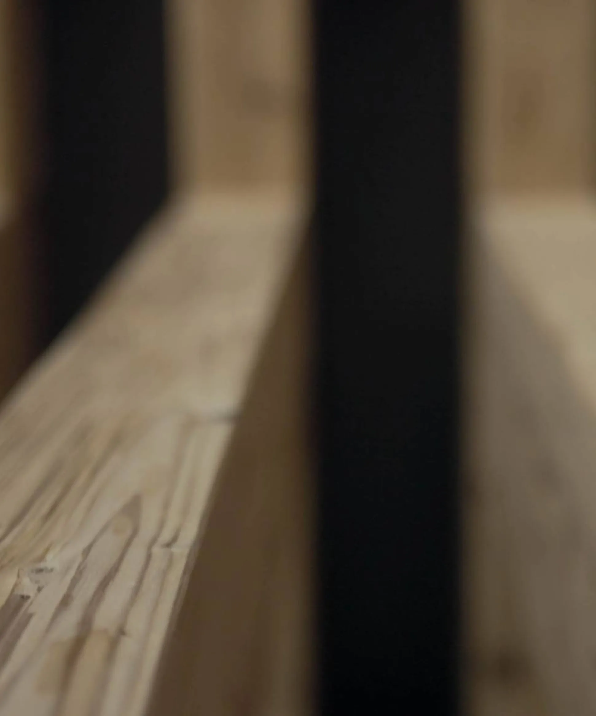 Primo piano di liste di legno chiare con venature evidenti, prospettiva verso una barra nera centrale e sfondo sfumato.