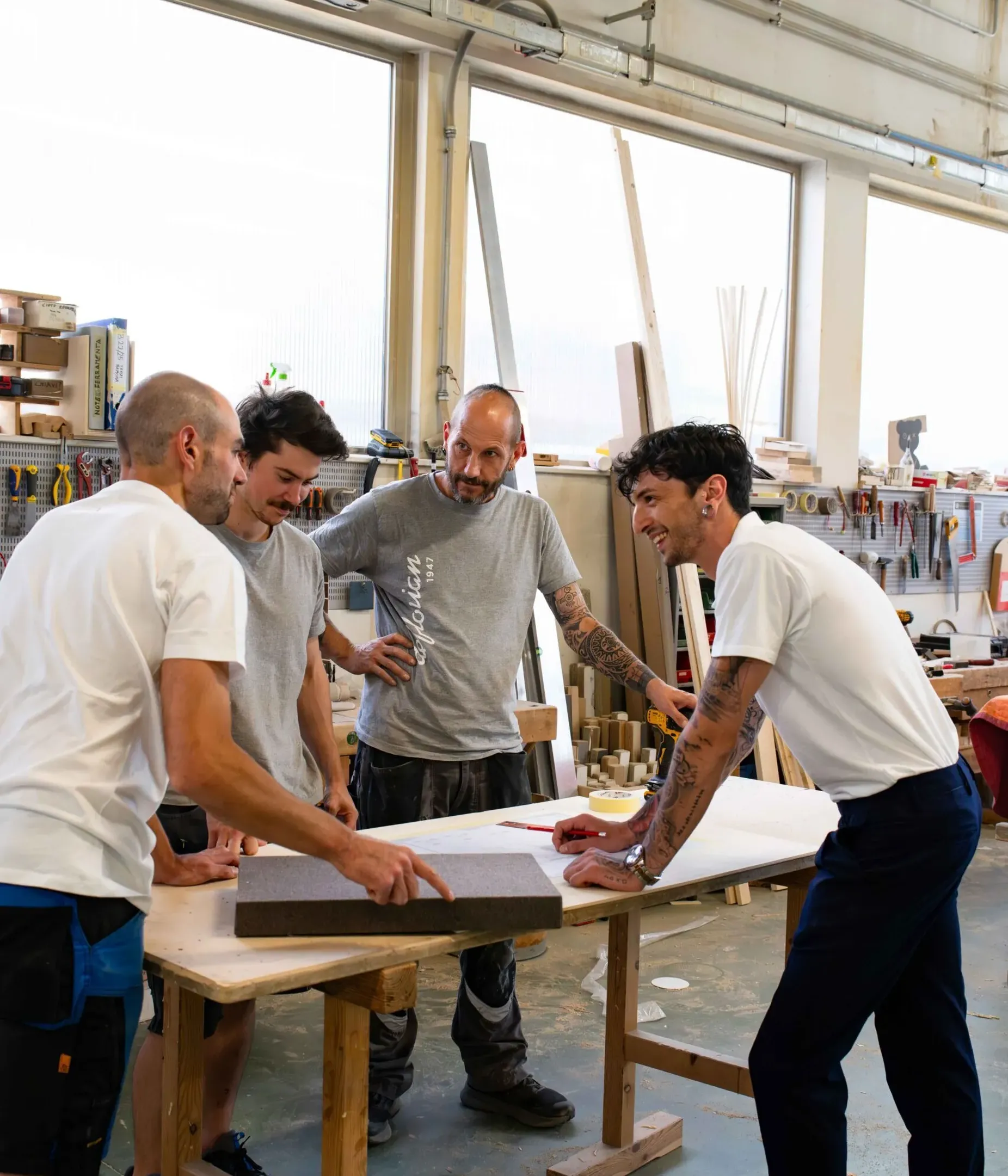 Quattro professionisti in un laboratorio Silenzia esaminano un pannello fonoassorbente appoggiato al tavolo, tra strumenti e scaffali.