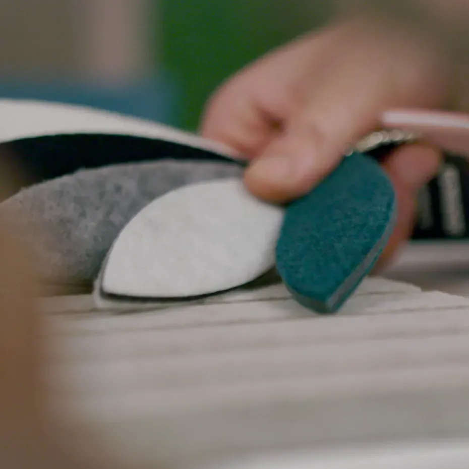 Primo piano: una mano sistema due dischi in schiuma, blu e bianco, su una superficie, durante un lavoro di installazione acustica Silenzia.