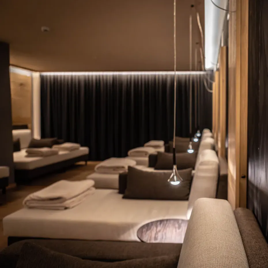 Sala lounge insonorizzata con divani bianchi, cuscini marroni, coperte piegate e tende nere; luci pendenti e pannelli acustici in legno sulle pareti.