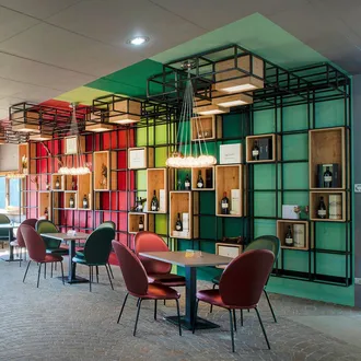 Showroom Silenzia: interno moderno con pareti a griglia colorate, scaffali in legno e bottiglie, tavoli e sedie vivaci, luce naturale.